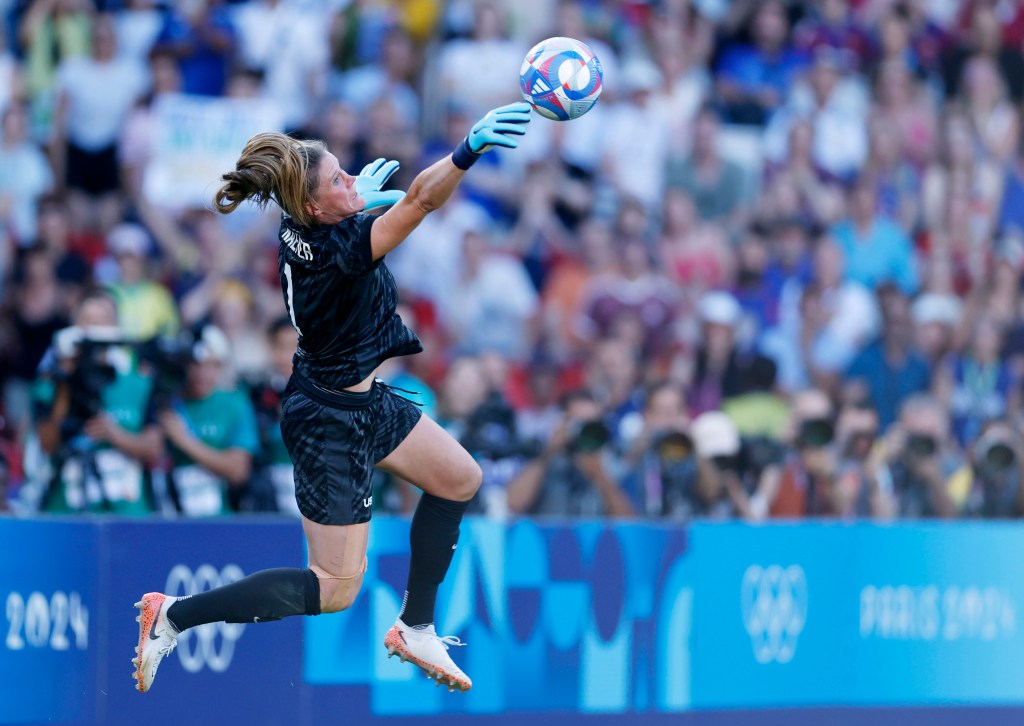 United States goalkeeper Alyssa Naeher is shown in midair and from the side as she leaps to her right to make a save with her glove.