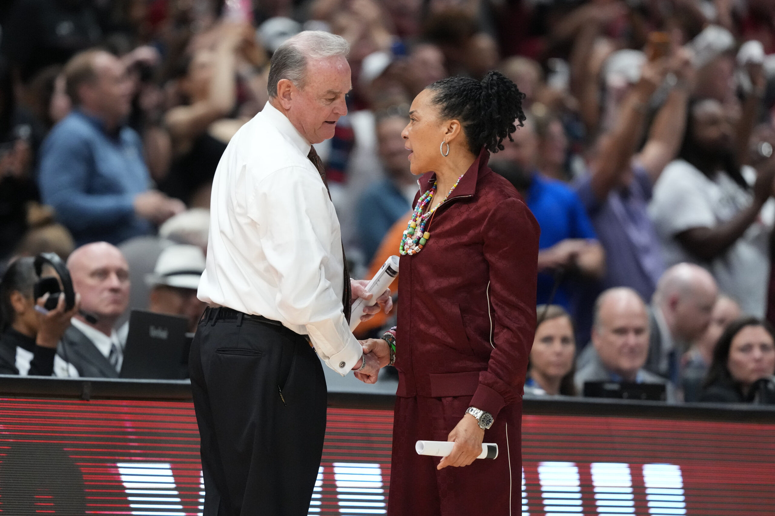 Texas head coach Vic Schaefer shakes hands with South Carolina head coach Dawn Staley on the sideline. Both are shown in profile, looking at one another.