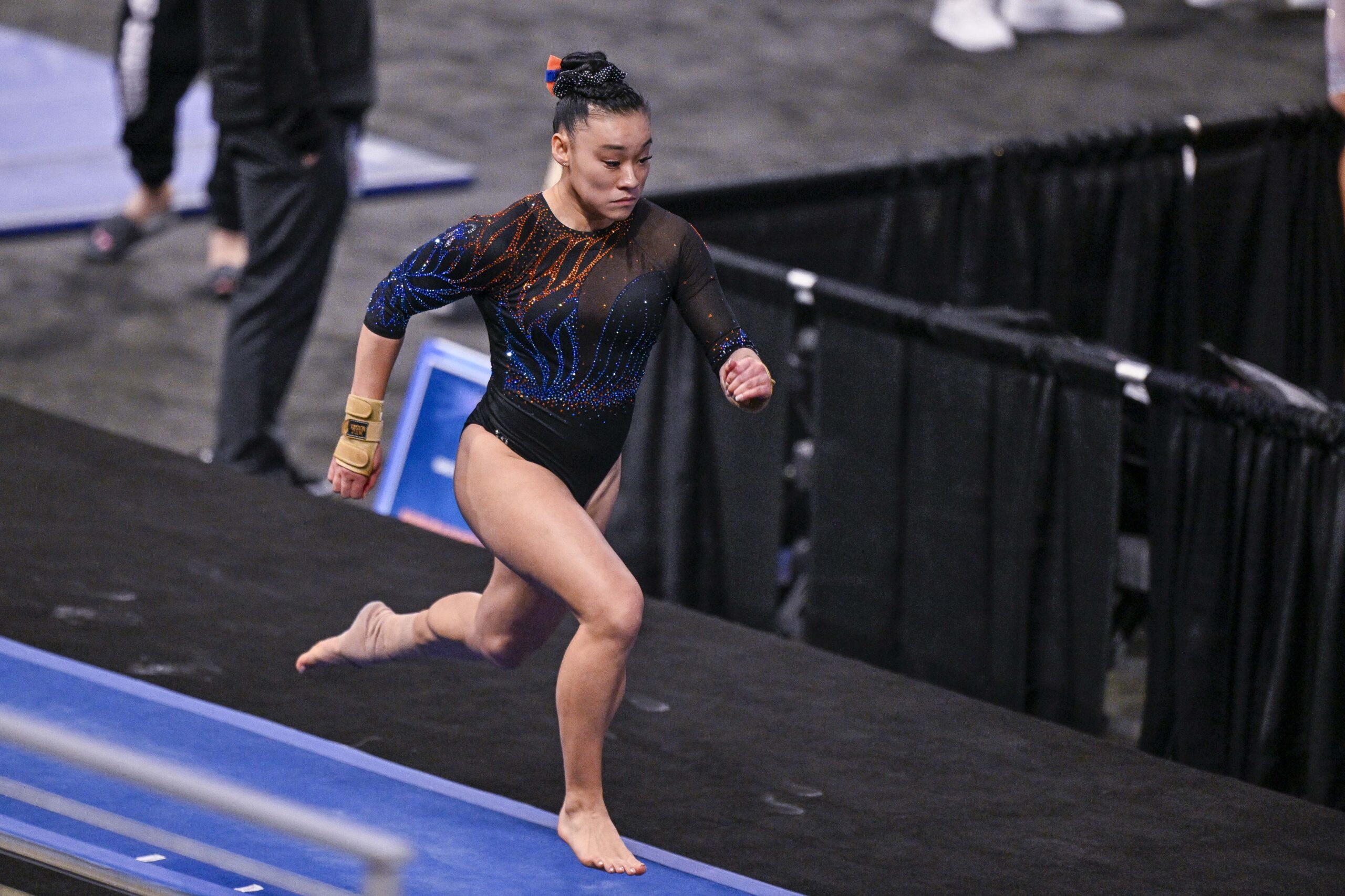 A gymnast in a black leotard runs on the vault runway.