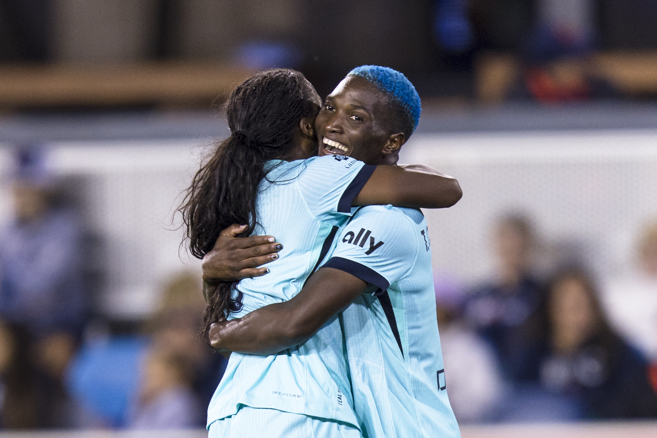 Two players in blue jerseys hug on a soccer field