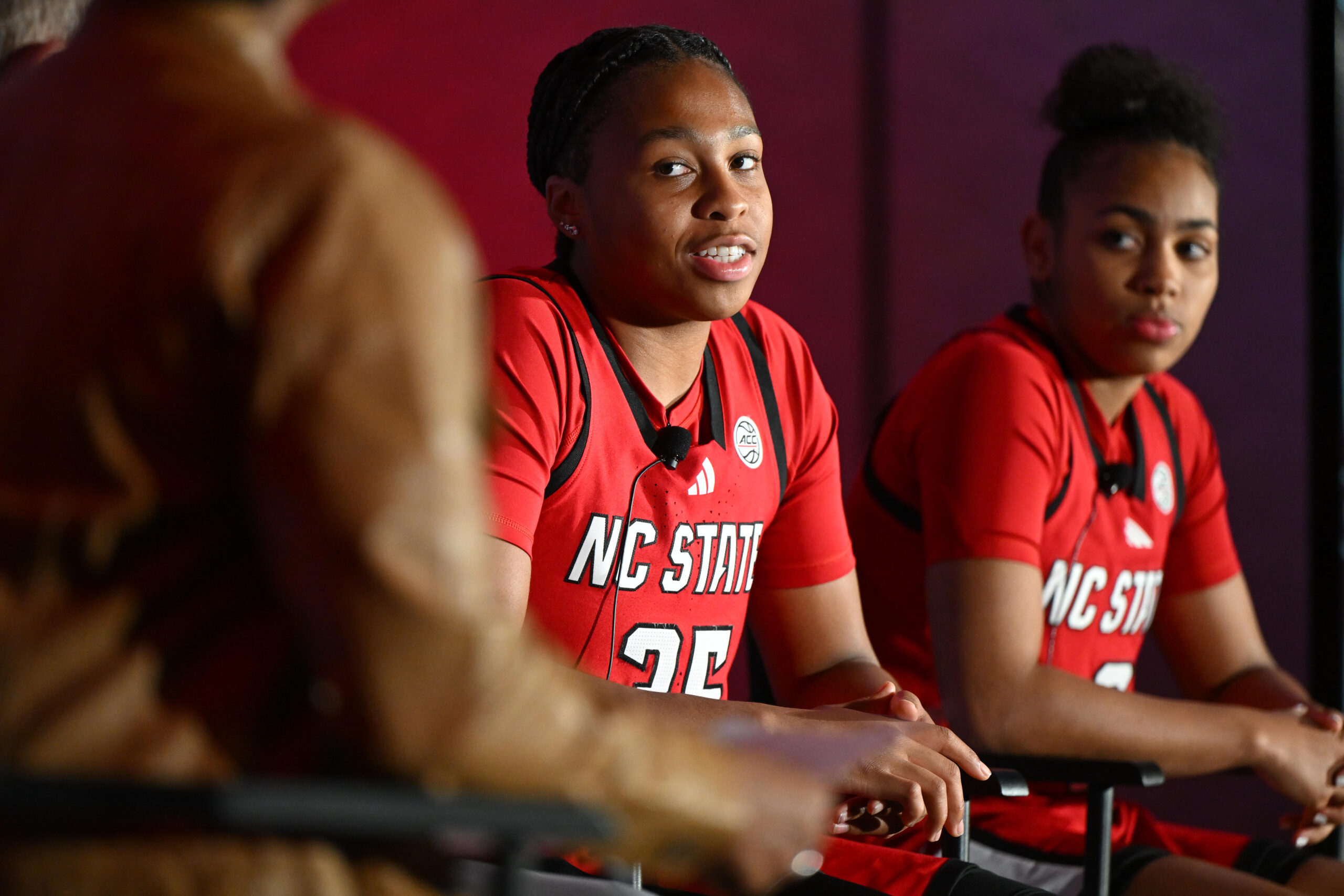 Zoe Brooks is facing toward the speaker and looking directly at them. She is wearing her red N.C. State jersey.