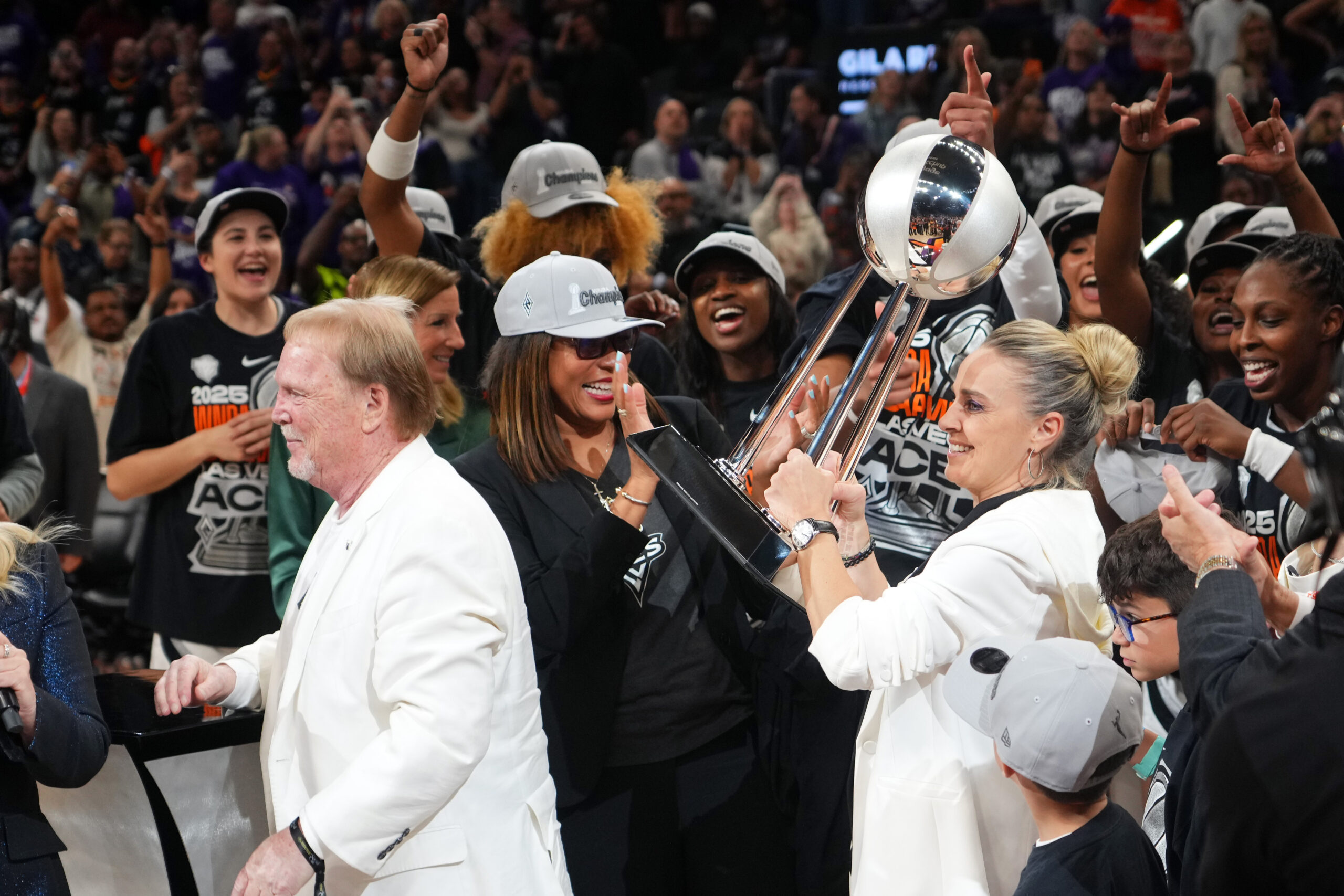 Becky Hammon holds up the 2025 championship trophy with team President Nikki Fargas celebrating with her. Mark Davis has his back turned to both Fargas and Hammon in the shot.