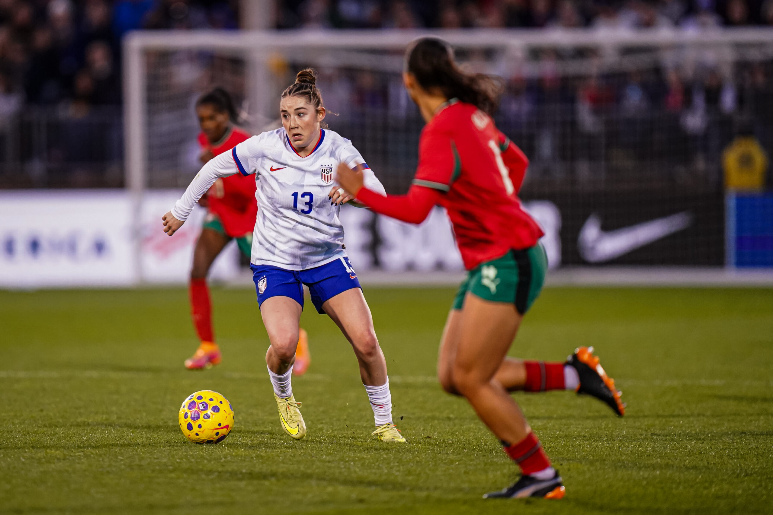 United States midfielder Olivia Moultrie is shown facing the camera, with the ball just off her right foot. She has her head up as a Portugal defender runs laterally to stay with her.