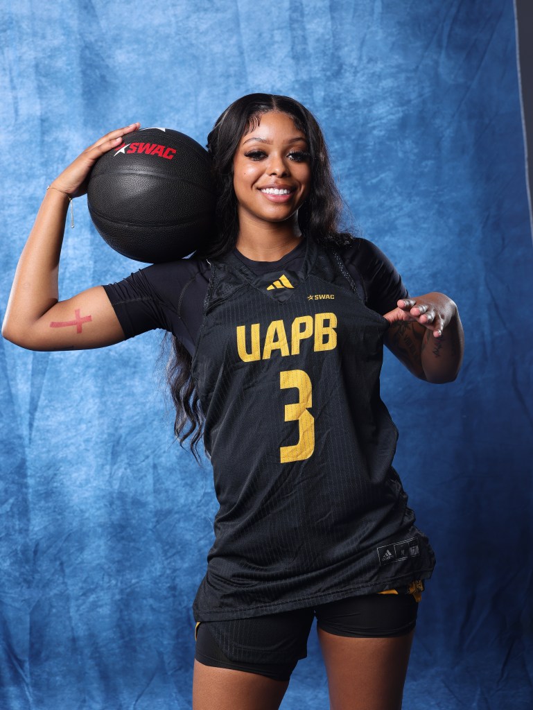 UAPB Indiya Bowen holds a black ball as she poses for a photo and smiles. She wears a black jersey that has the UAPB letters on it.