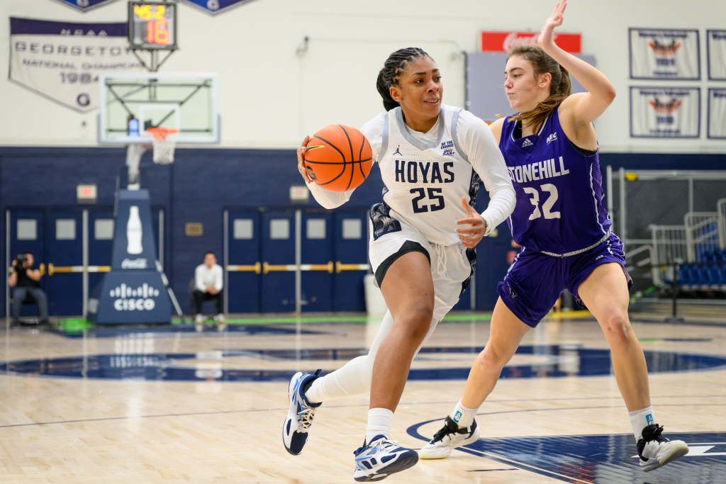 Georgetown forward Chet Nweke dribbles the ball with her right hand just outside the lane. Stonehill forward Julia Webster slides her feet to try to stay with her.