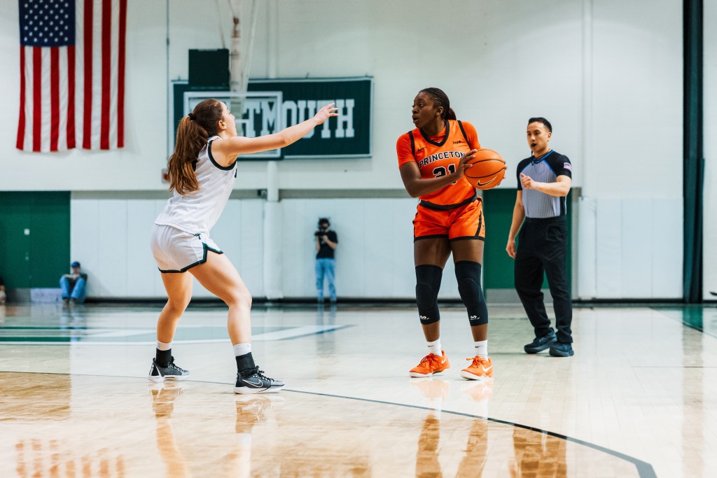 Princeton guard Toby Nweke holds the ball with two hands near her left hip. She is standing behind the 3-point line and looking across the court.