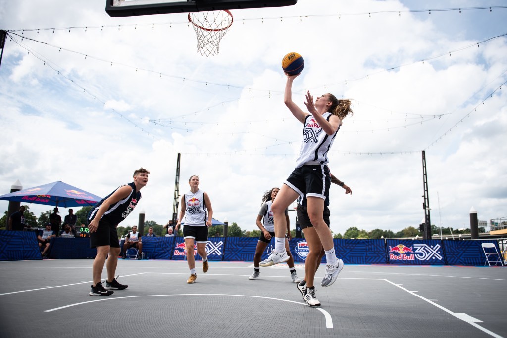 Blake Dietrick-Seifert shoots an open right-handed layup on the left side of the basket in a 3x3 game. Teammate Camille Zimmerman runs down the lane unguarded, ready to rebound if needed.