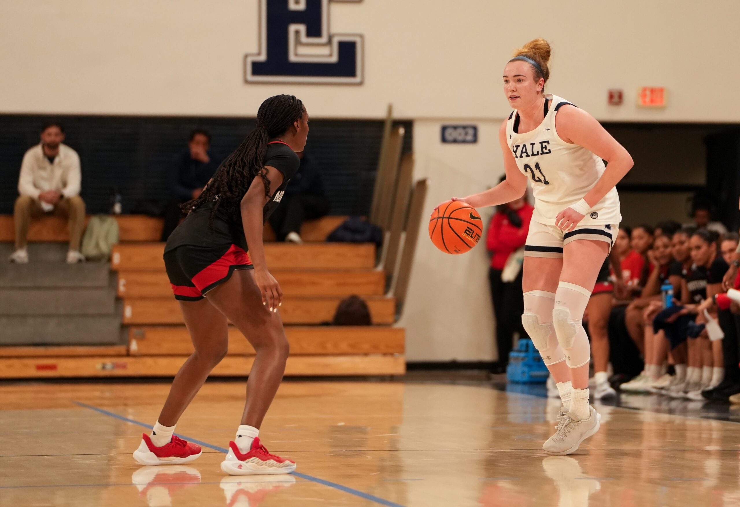 Yale guard Kiley Capstraw dribbles the ball with her right hand and scans the court. A Northeastern defender is in front of her but not guarding her very tightly.