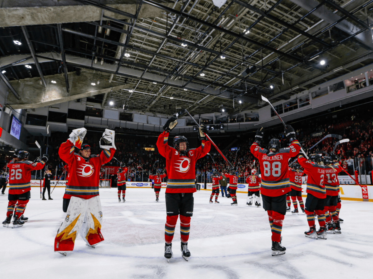 Charge players stand around the center ice circle, raising their arms in their post-game celebration tradition at TD Place. They are wearing red home uniforms.