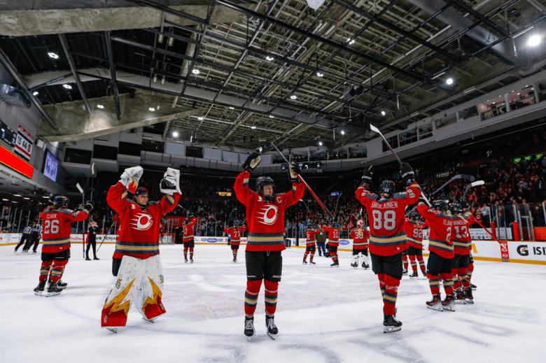 Charge players stand around the center ice circle, raising their arms in their post-game celebration tradition at TD Place. They are wearing red home uniforms.