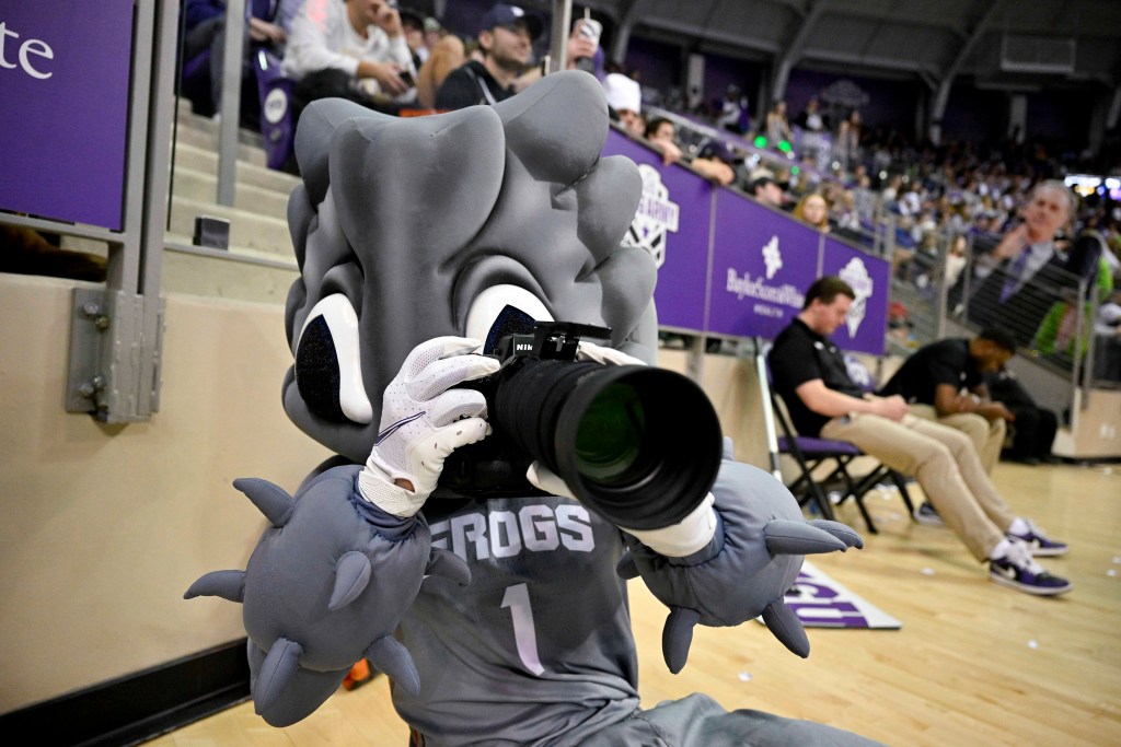 The TCU mascot points a large camera on the baseline at a TCU basketball game.
