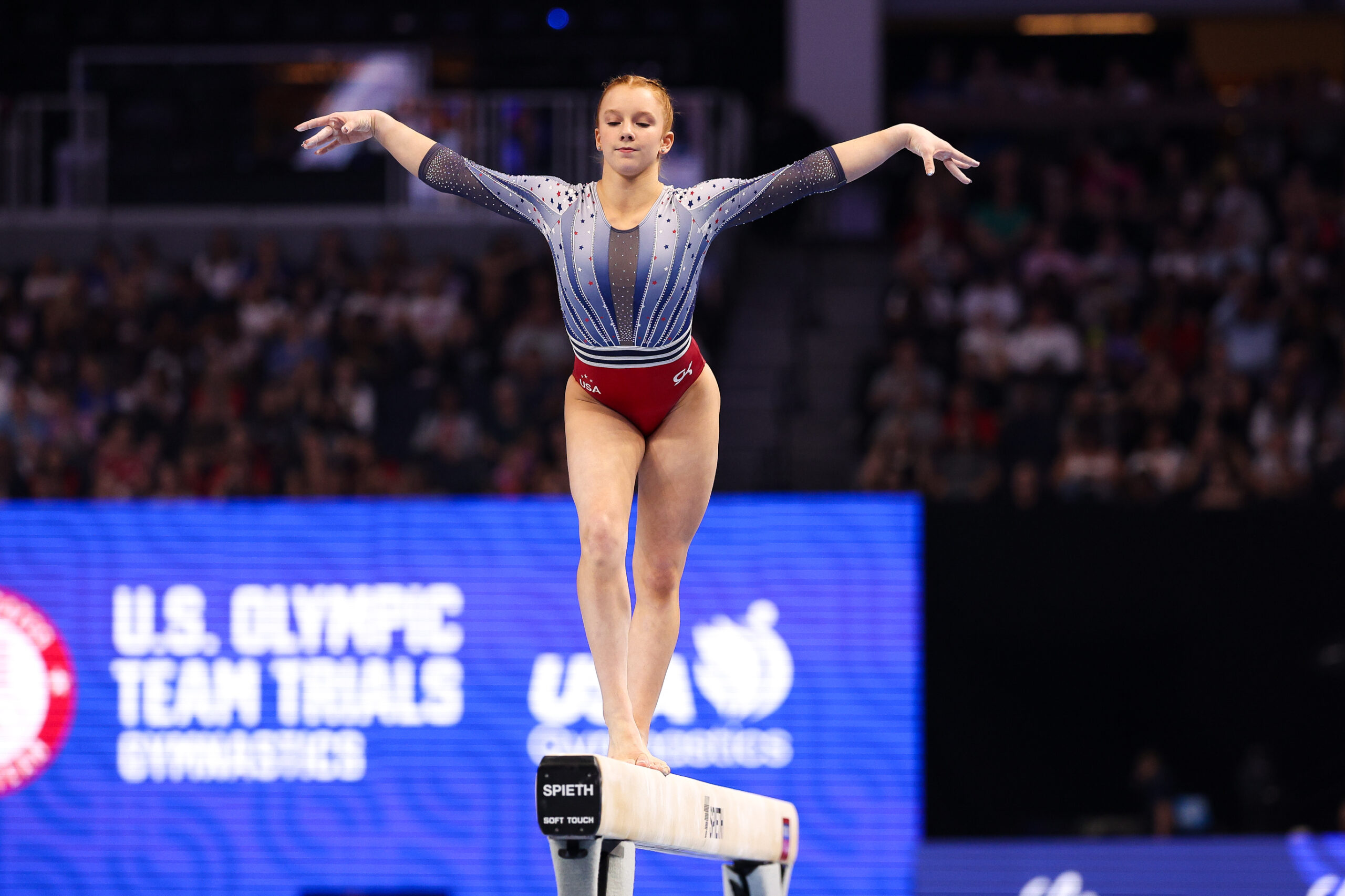 A gymnast in a red, white, and blue leotard performs on the balance beam.