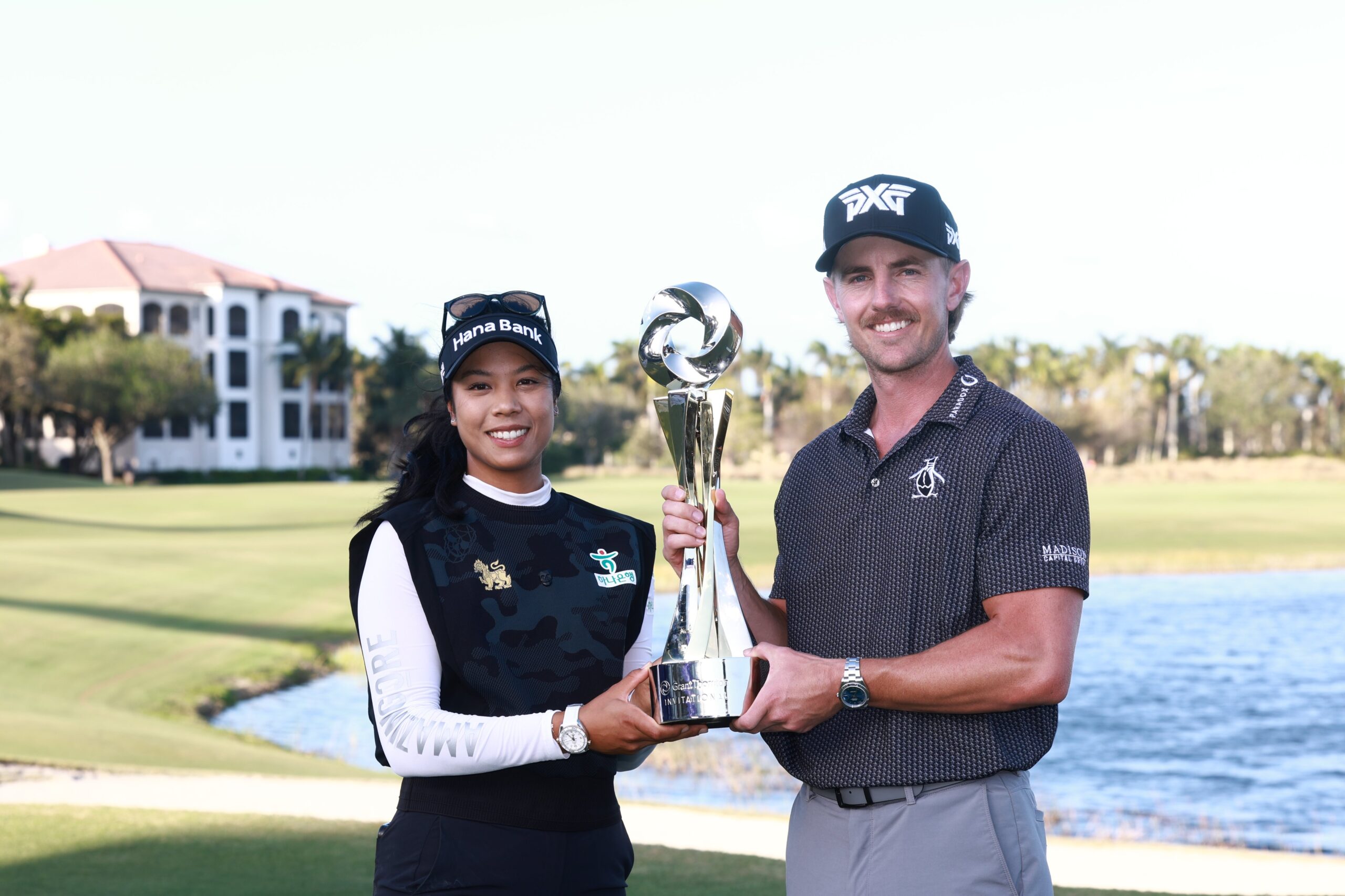 Patty Tavatanakit and Jake Knapp both hold the Grant Thornton Invitational trophy in the middle of them. Tavatanakit has her right hand on the bottom of the trophy and her left behind it, and Knapp has his left hand on the bottom and right hand around the trophy's top. The pond and fairway of Tiburón Golf Course stretch behind the players.