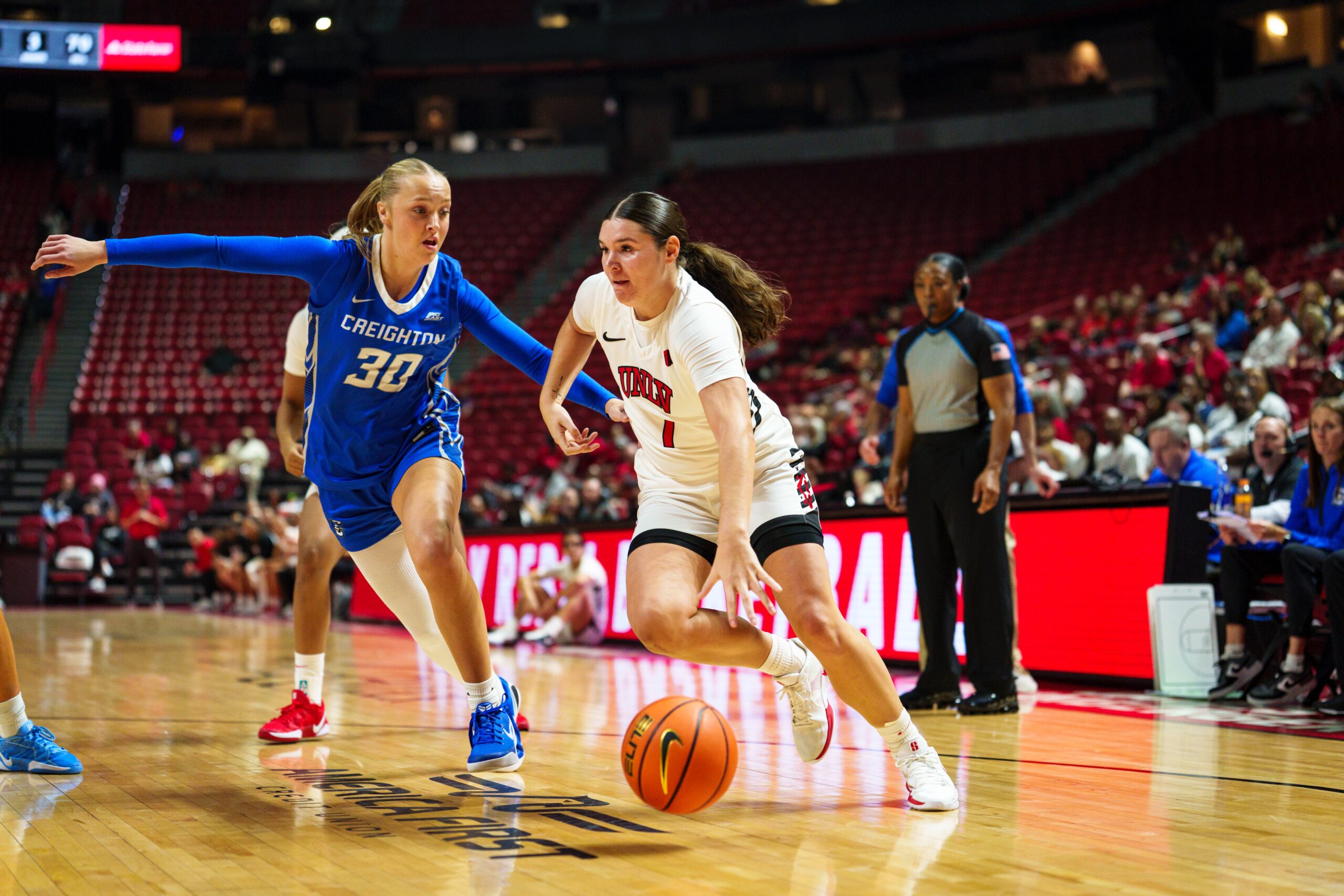Two players battle for a basketball on a court. The player on the left is in a blue uniform and the player on the right is in a white uniform.