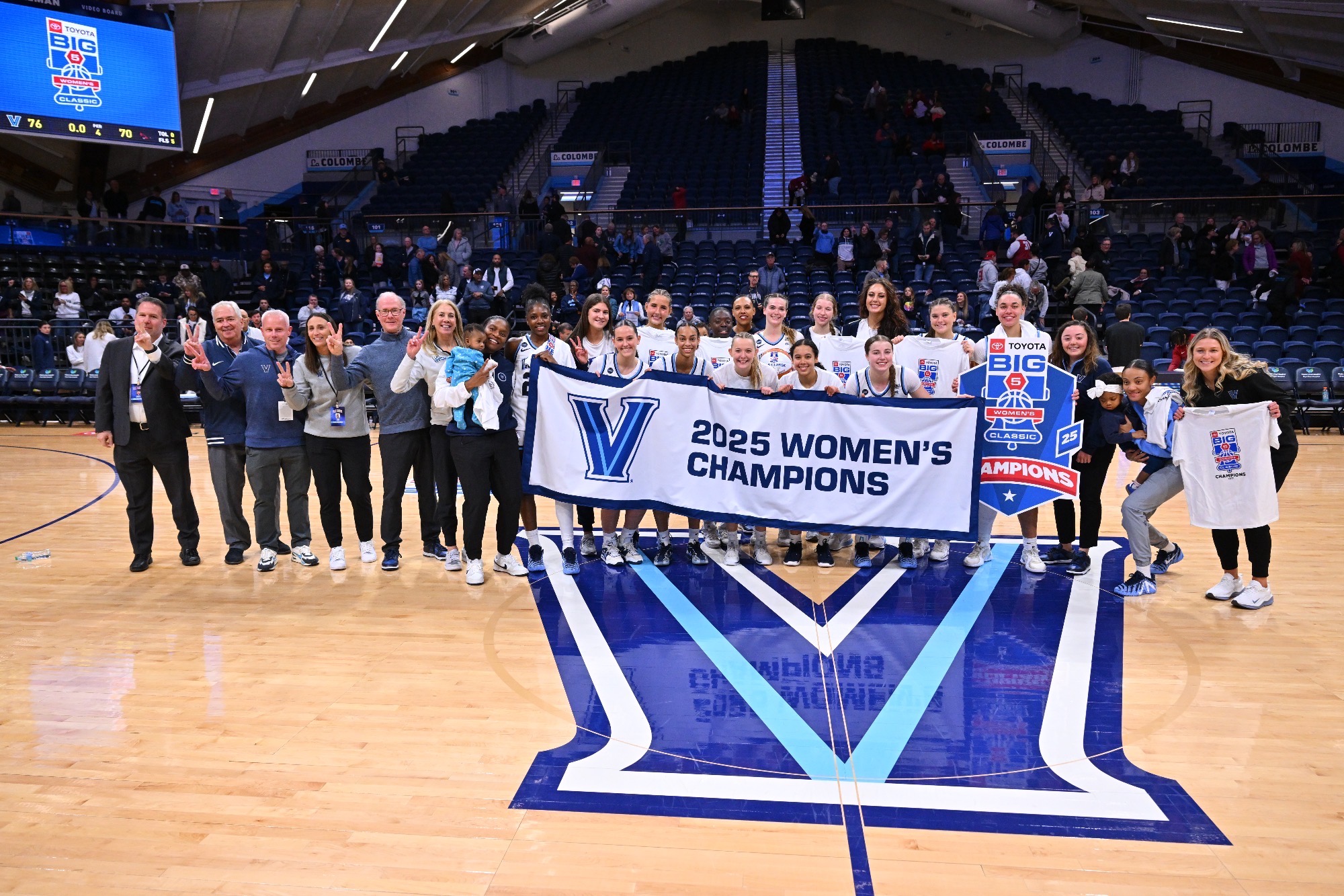 The Villanova women's basketball teams stands on a basketball court with a banner that reads "2025 women's champions"