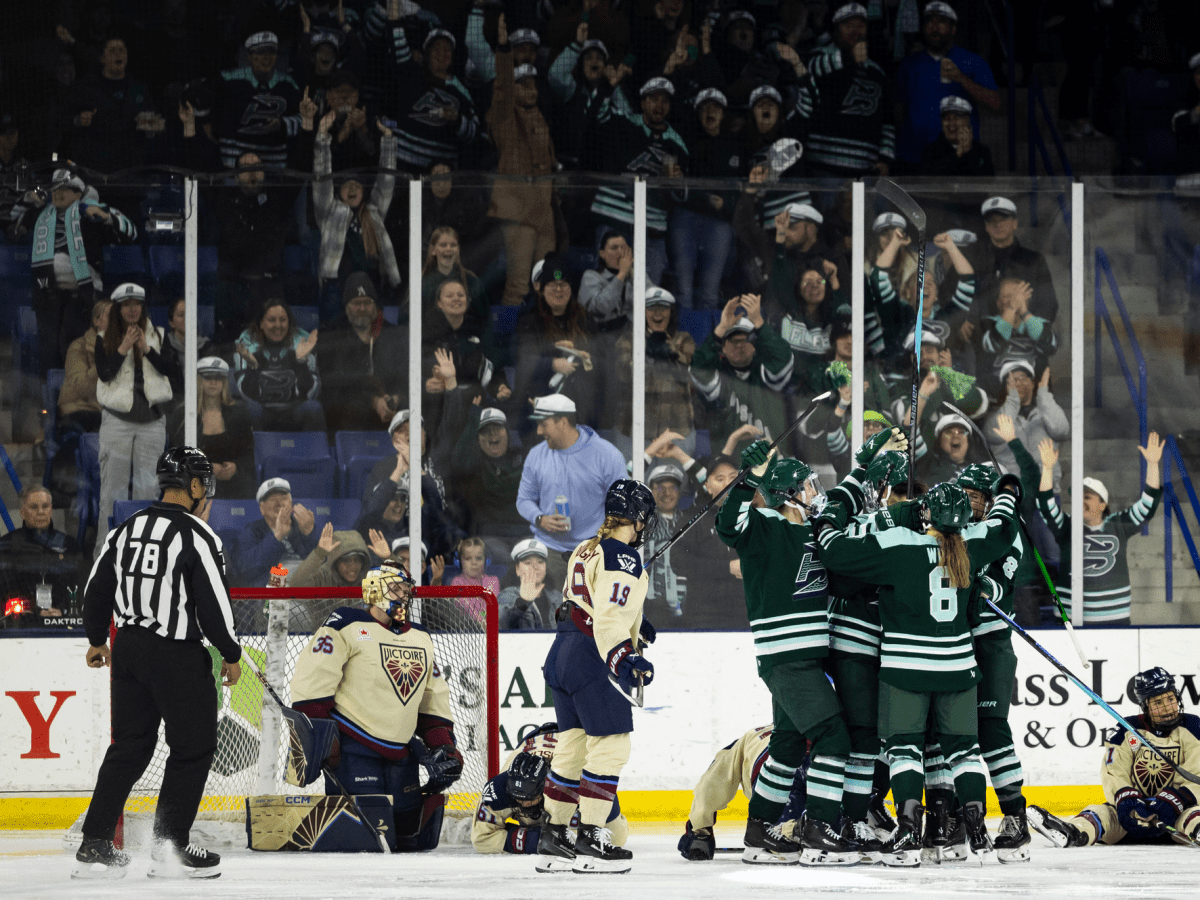 The Fleet celebrate with a group hug by the Montréal net. Cheering fans are in the background. The Fleet are wearing green home uniforms, while the Victoire are in cream away ones.