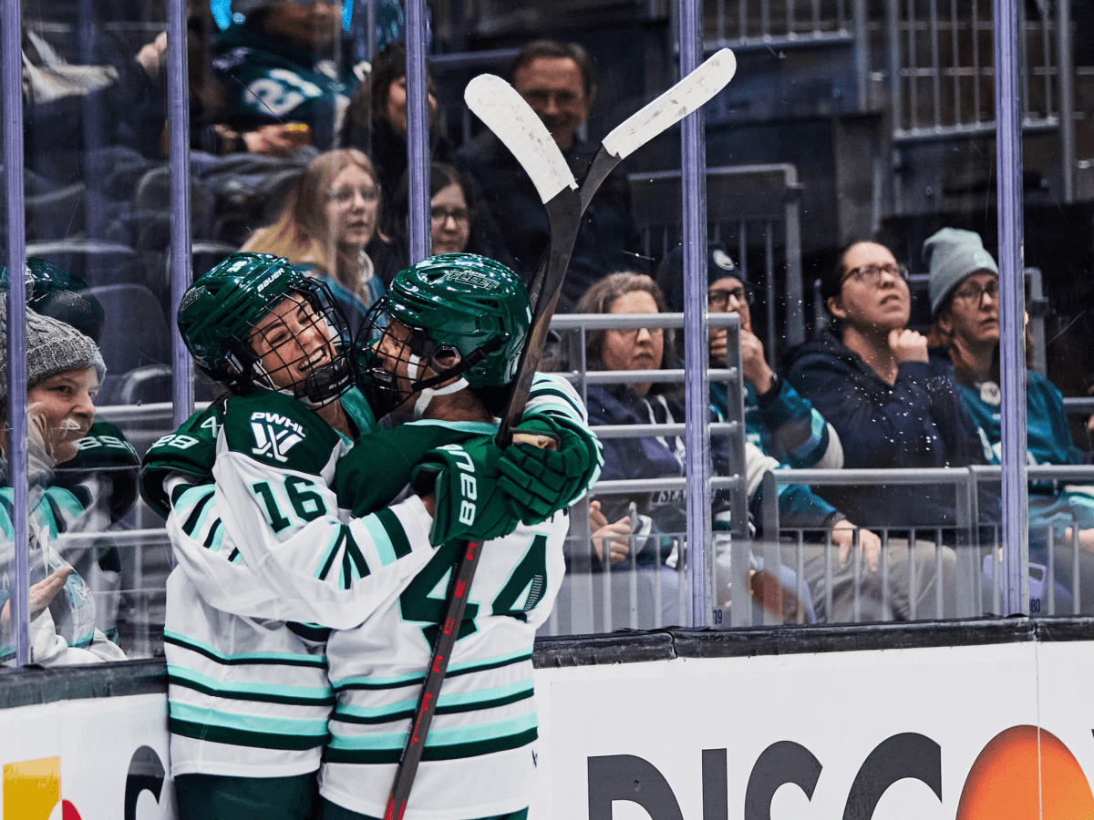 Brengman and Saulnier smile as they hug in the corner. They are both wearing white away uniforms.