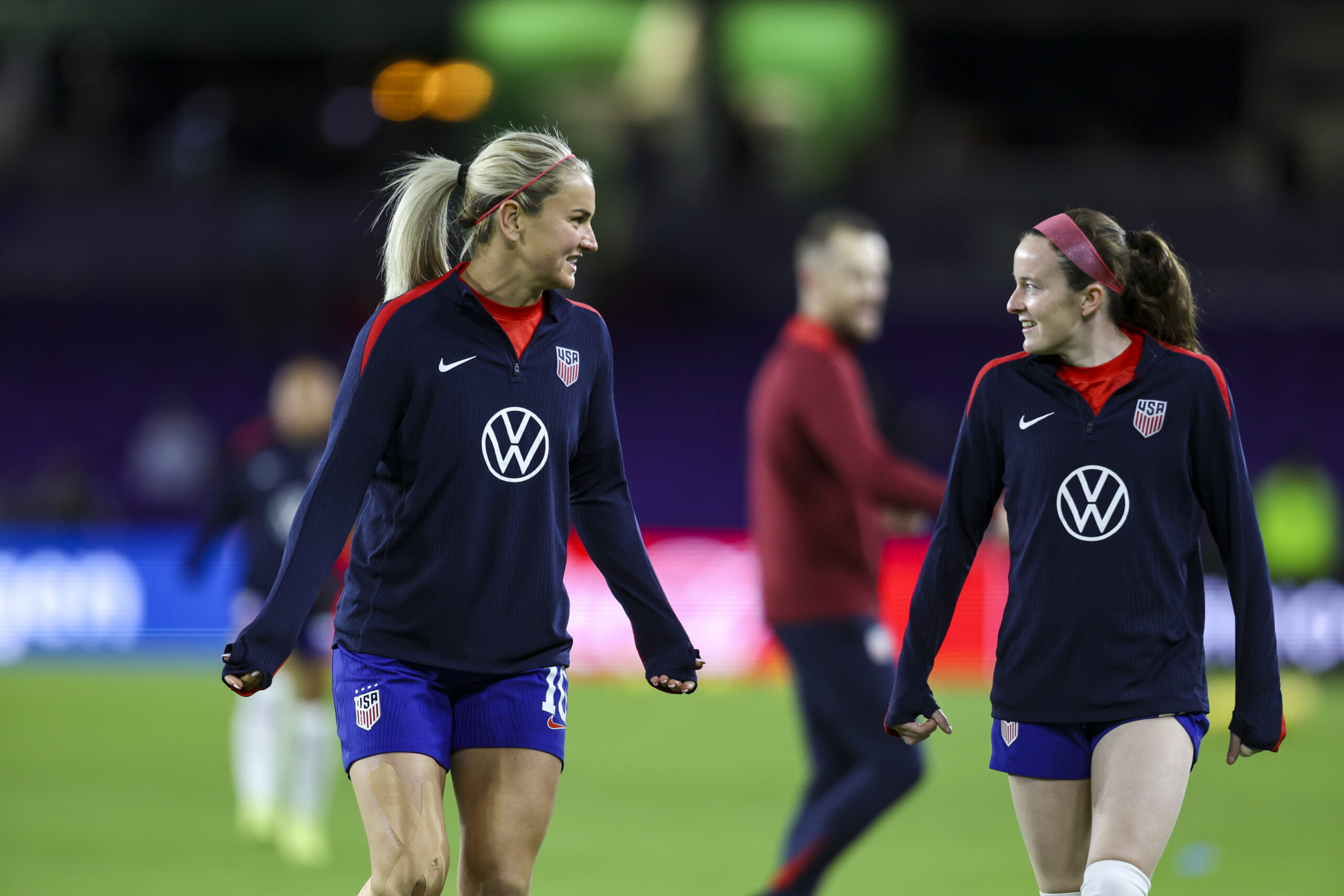 Two players in USWNT uniforms walk on the field