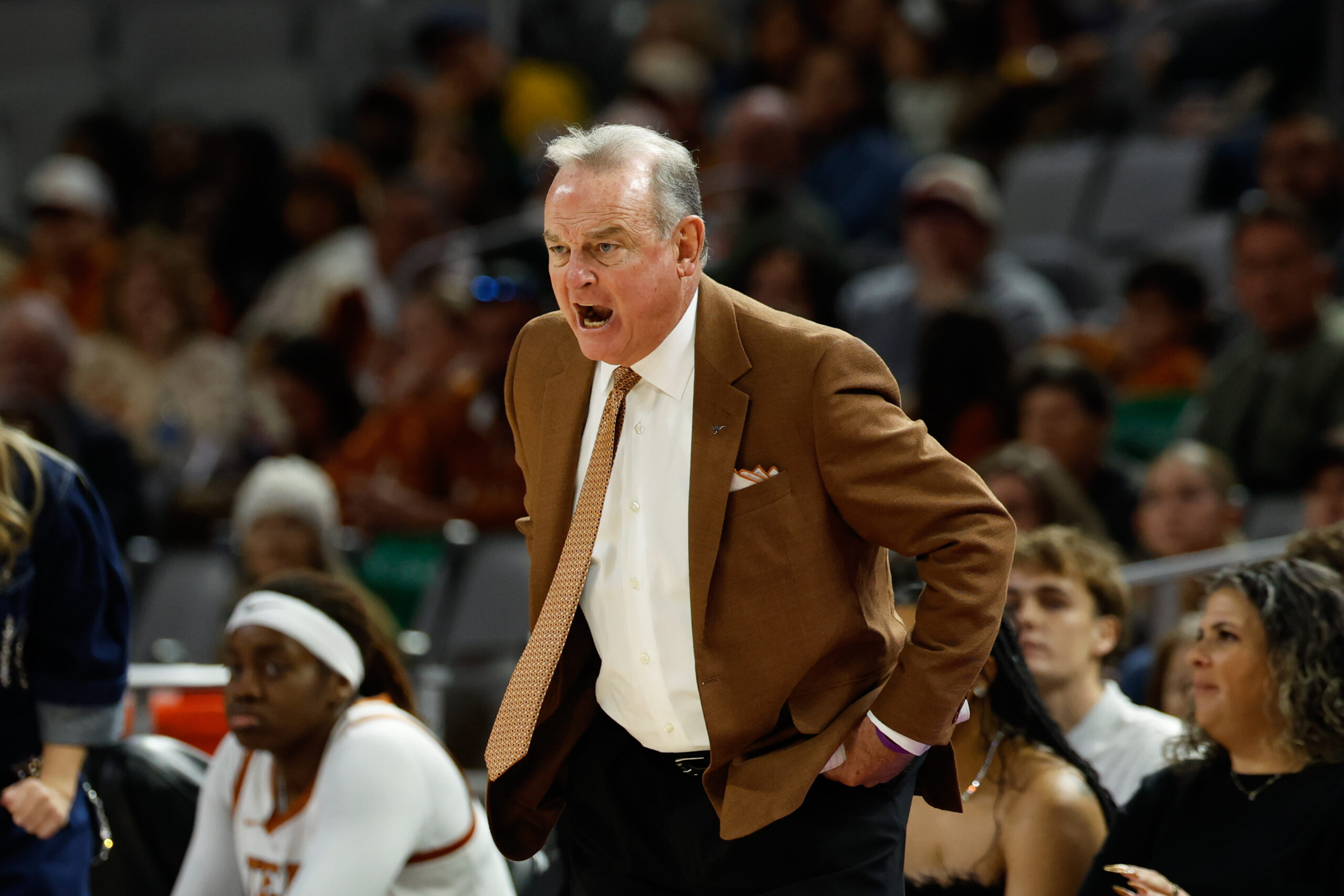 Texas head coach Vic Schaefer stands on the sideline yelling with his hands on his hips while wearing an orange tie and brown suit jacker