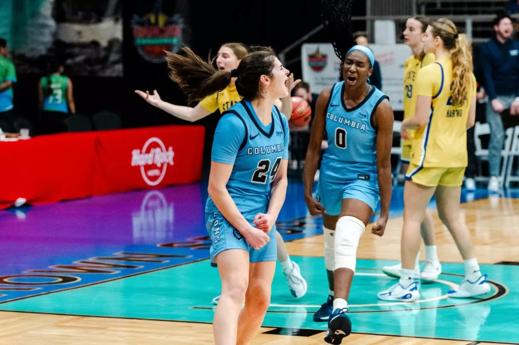 Columbia guard Riley Weiss and forward Susie Rafiu clench their fists and shout in celebration during a game. Weiss is closest to the camera, and Rafiu is walking toward her. In the background, a South Dakota State player puts her hands up in disbelief.