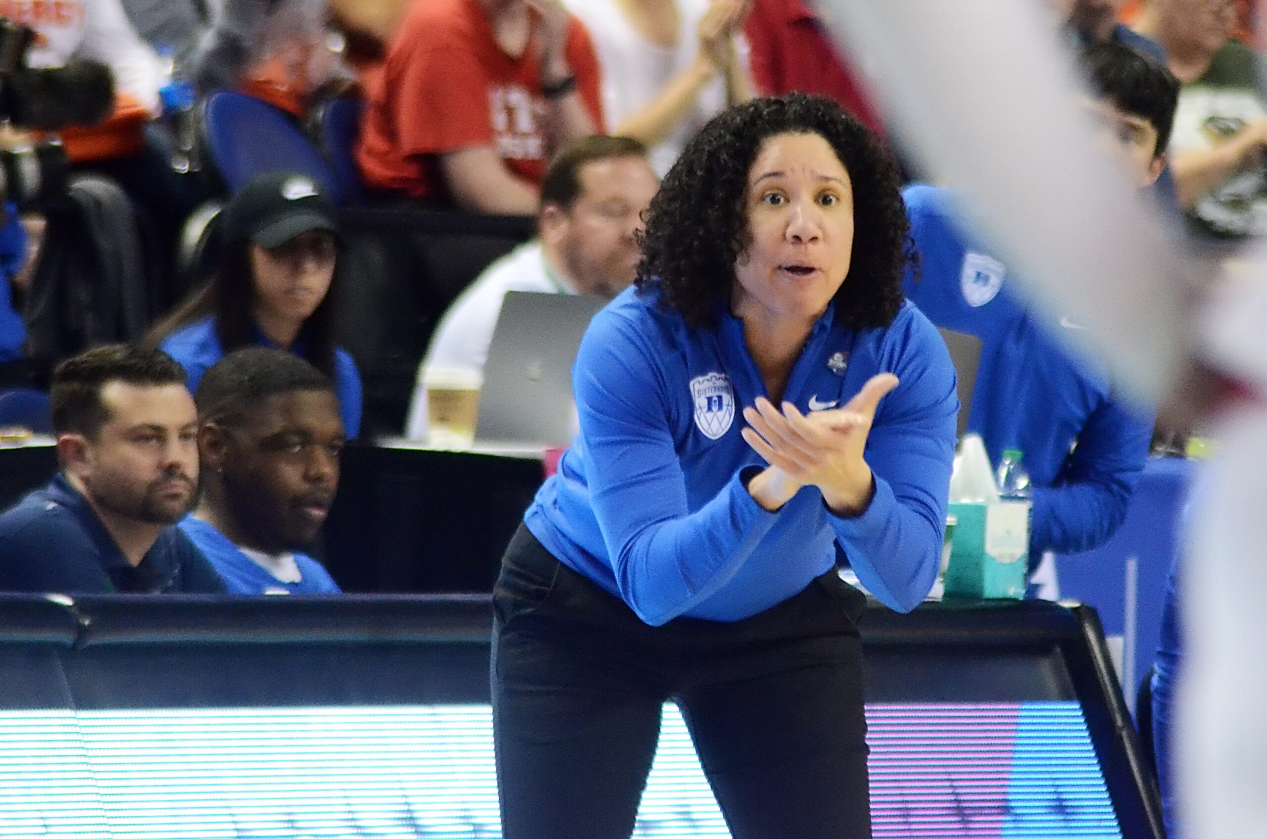 Duke head coach Kara Lawson stands slightly bent over, clapping her hands from the sideline.
