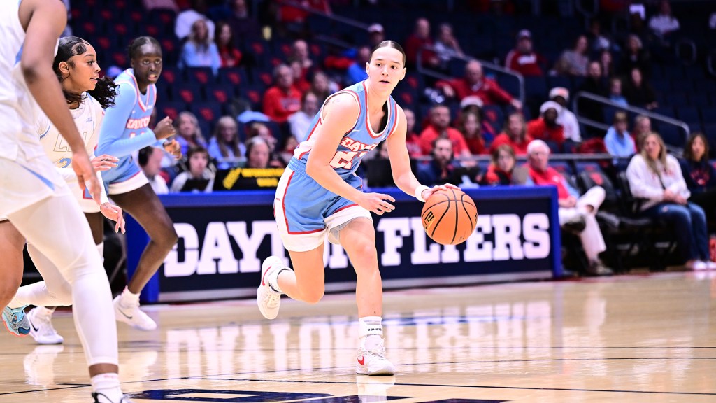 Dayton graduate student guard Nicole Stephens dribbles the ball with her left hand and looks to create a path around a defender. Her right leg is bent at a 90-degree angle as she runs and looks down the court.