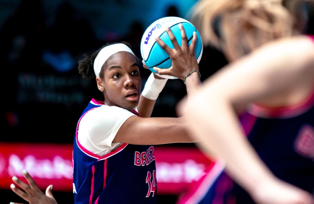 A player wearing a blue and white jersey holds a basketball on the court