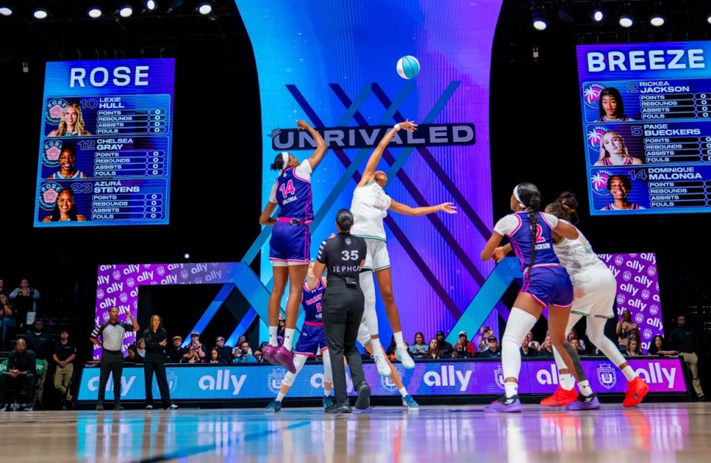 Players jump for the ball on the Unrvaled court. Two of the players in the frame wear white jerseys, and three wear purple.