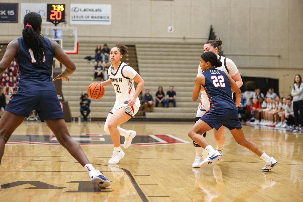 Brown guard Grace Arnolie dribbles the ball with her left hand just outside the lane. Her eyes are up, as if looking at the basket, and her closest defenders are a few steps away.