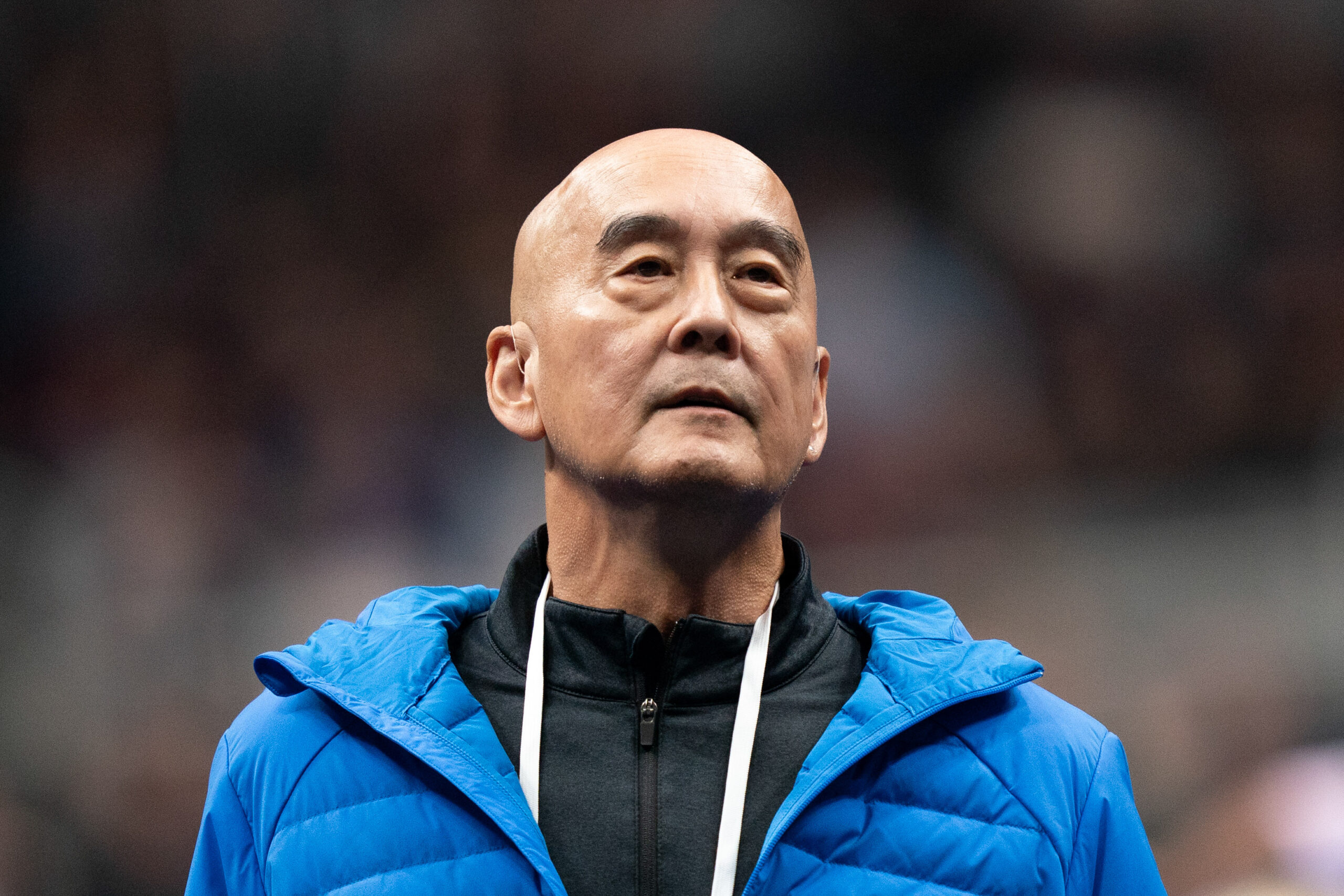 Coach Al Fong, wearing a blue hoodie and a white lanyard, looks into the distance at the 2023 US Gymnastics Championships.