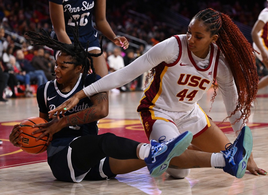 Gabby Elliott and Kiki Iriafen vie for the ball on the court. Iriafen, in a white USC Trojans uniform, is reaching for the ball while Elliott, in a navy Penn State uniform, secures it.