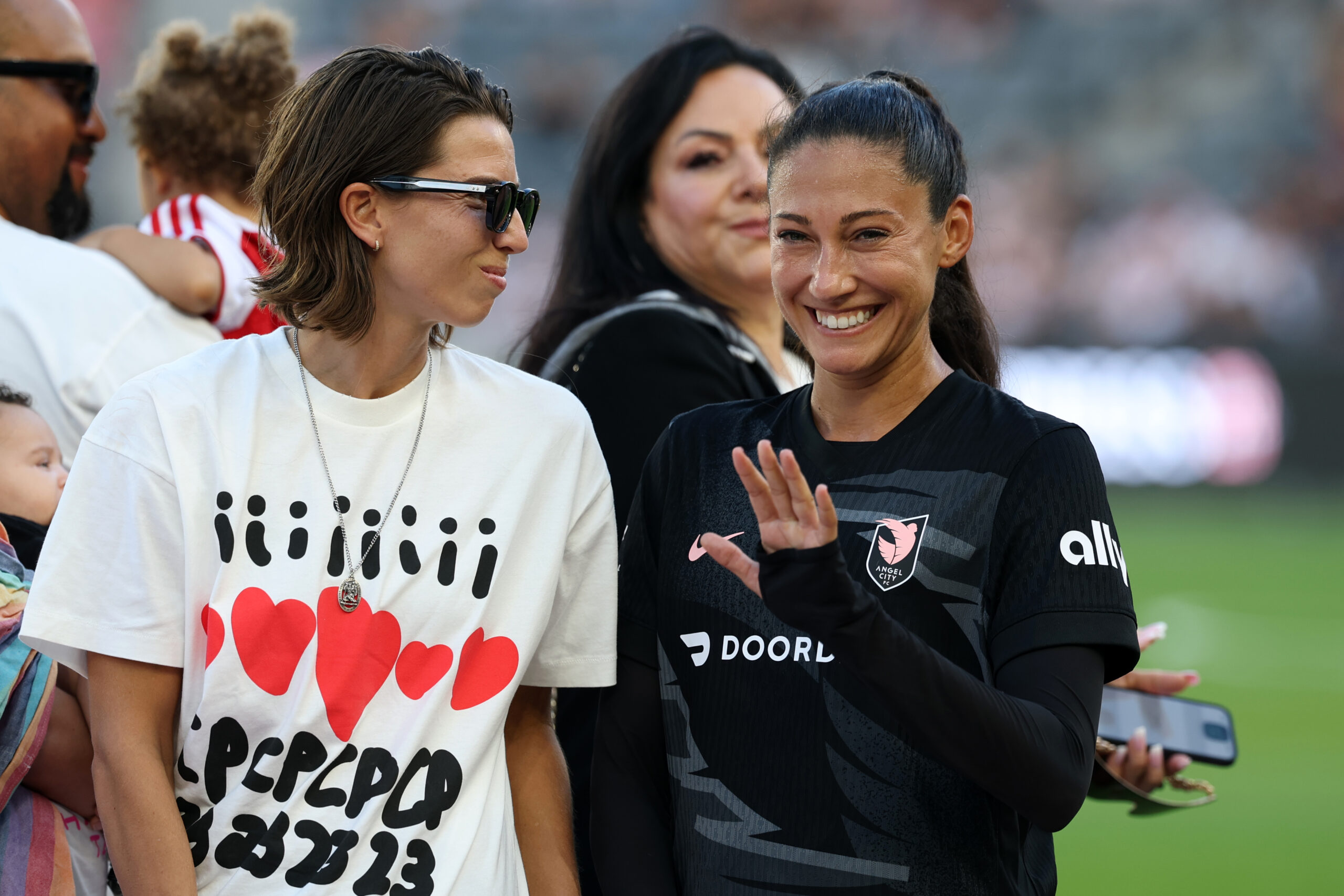 Tobin Heath standing next to Christen Press. Press is waving.
