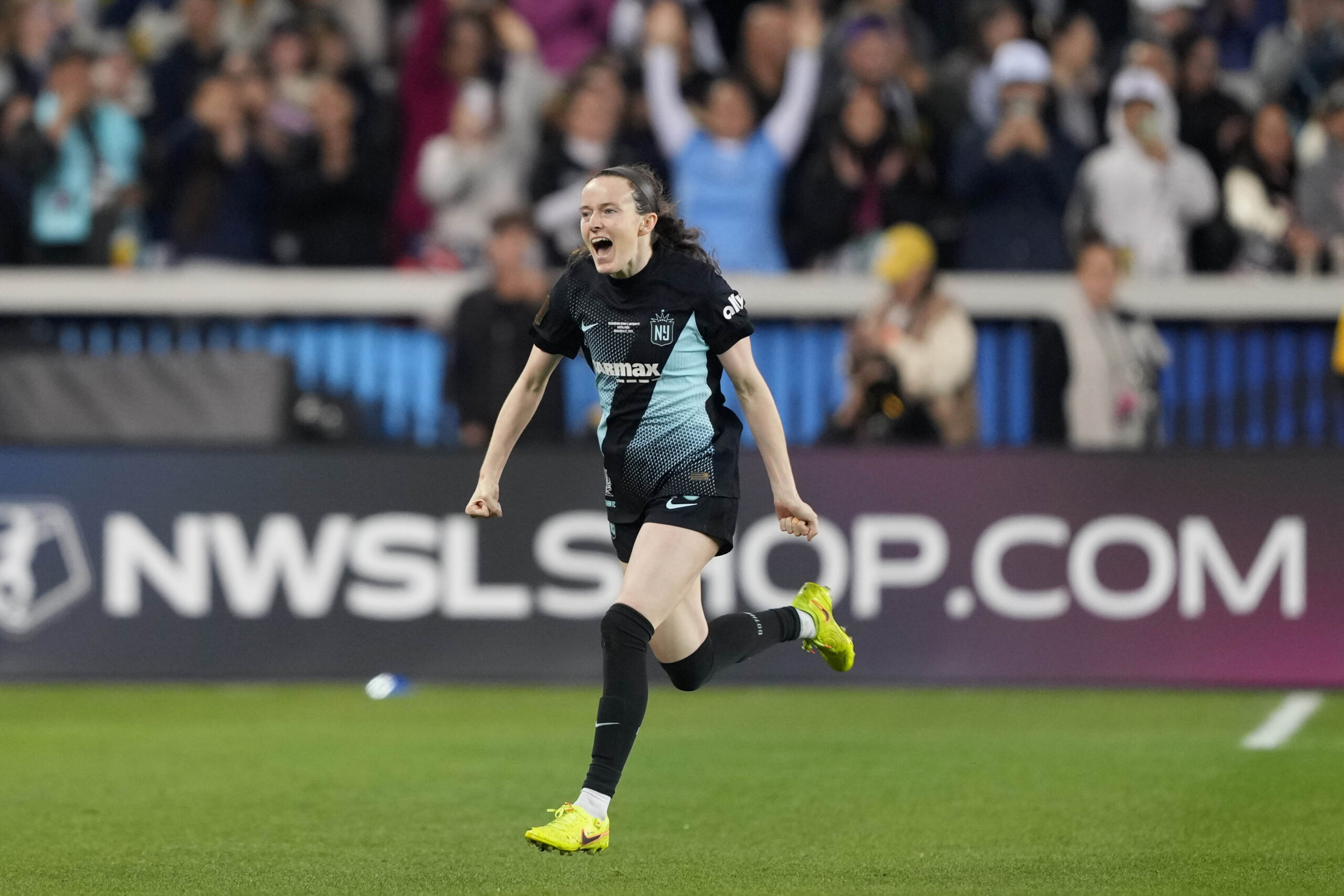 Rose Lavelle runs with her hands extended to her sides, celebrating scoring a goal.