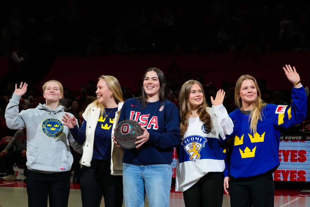 Five Ohio State women's ice hockey players stand side-by-side wearing the jerseys of their respective countries as they are honored during an Ohio State men's basketball game. From left to right: Hilda Svensson (Sweden), Jenna Raunio (Sweden), Joy Dunne (USA), Sanni Vanhanen (Finland) and Mira Jungåker (Sweden).