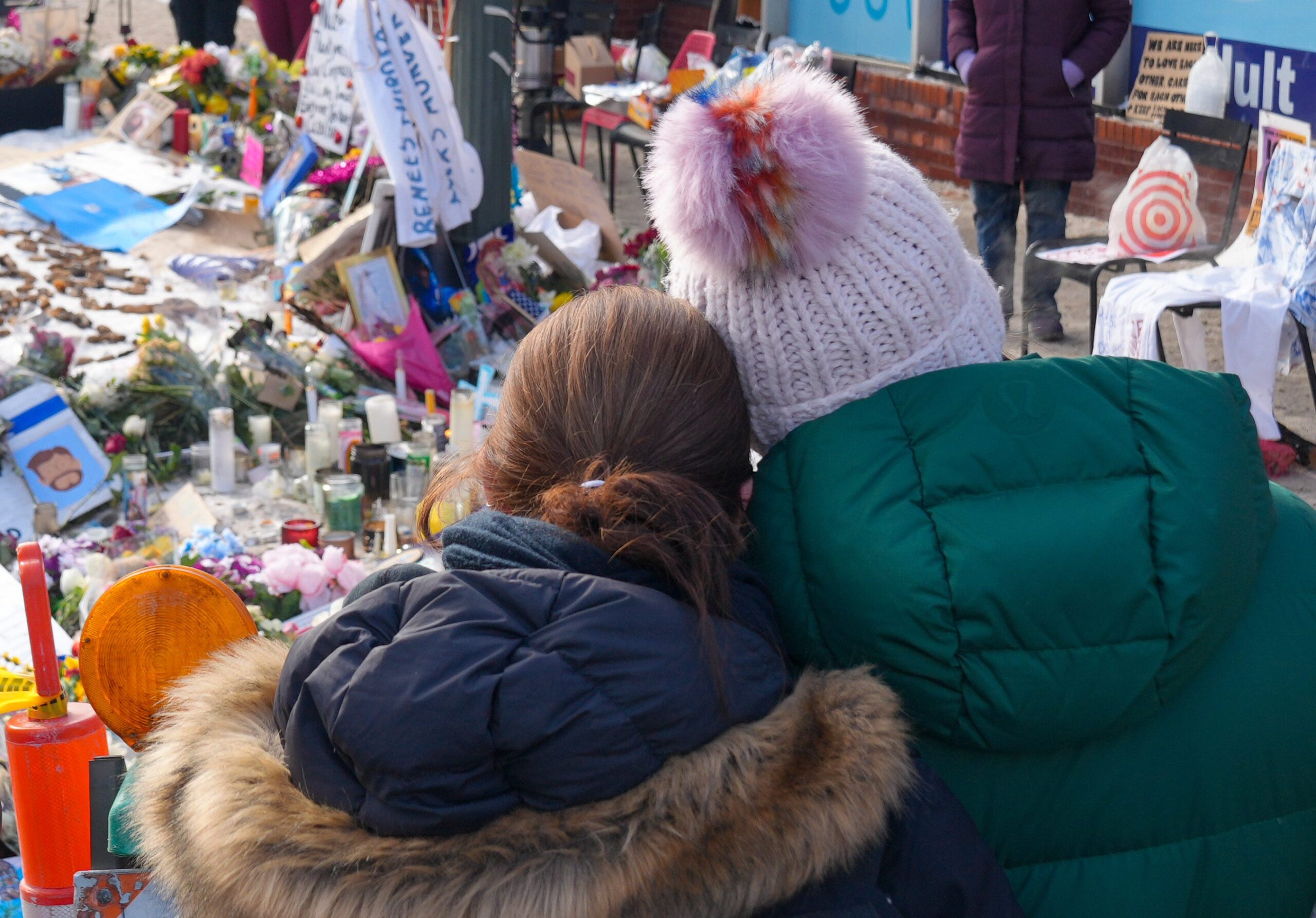 Two mourners facing a memorial lean their heads against each other