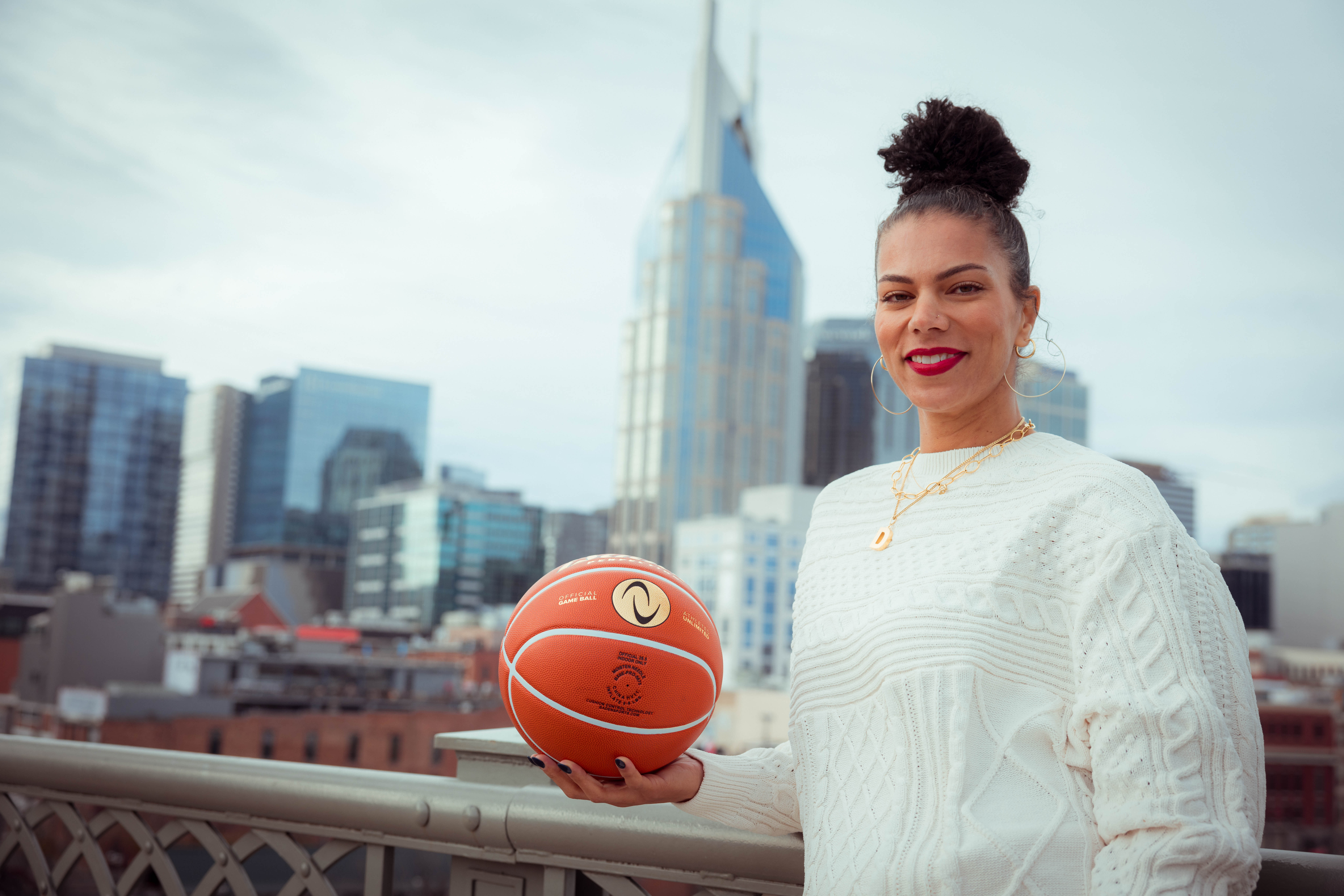 Alysha Clark poses with a basketball in her right hand in front of the Nashville skyline.