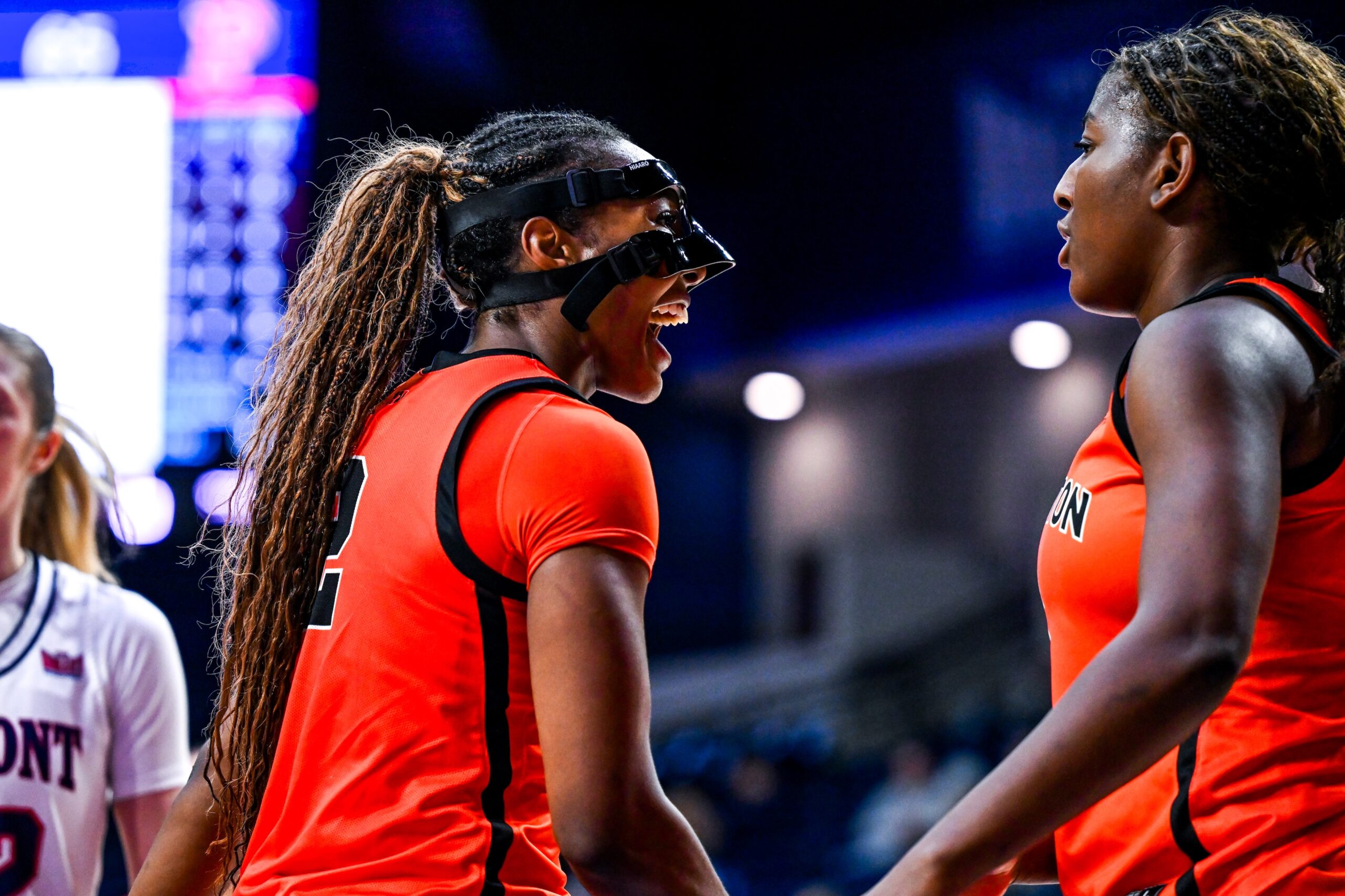 Princeton guard/forward Olivia Hutcherson is shown from the side, with a black mask covering her forehead, nose and cheekbones. She yells in celebration in the direction of guard/forward Fadima Tall.
