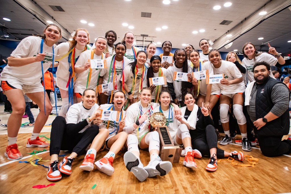The Princeton Tigers pose for a photo with their cardboard NCAA Tournament “tickets” after winning the 2024 Ivy League Tournament. Some of them are holding pieces of the net or holding up one finger, and many of them have rainbow streamers draped around their necks.