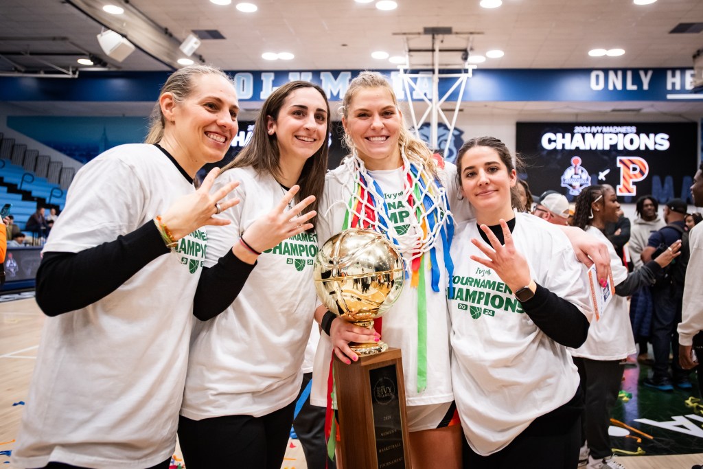 Princeton head coach Carla Berube, associate head coach Lauren Gosselin, forward Ellie Mitchell and assistant coach Lauren Dillon smile for a photo. Mitchell is holding the Ivy League championship trophy, and the coaches are each holding up four fingers after winning four regular-season titles in as many seasons.