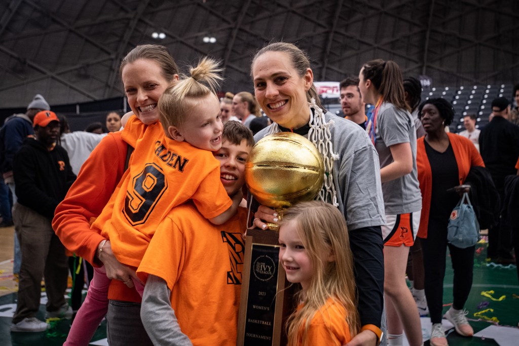 Princeton head coach Carla Berube helps two of her children hold up the Ivy League Tournament trophy. Berube’s wife, Meghan, stands next to Berube and holds their third child as the family smiles for a photo.