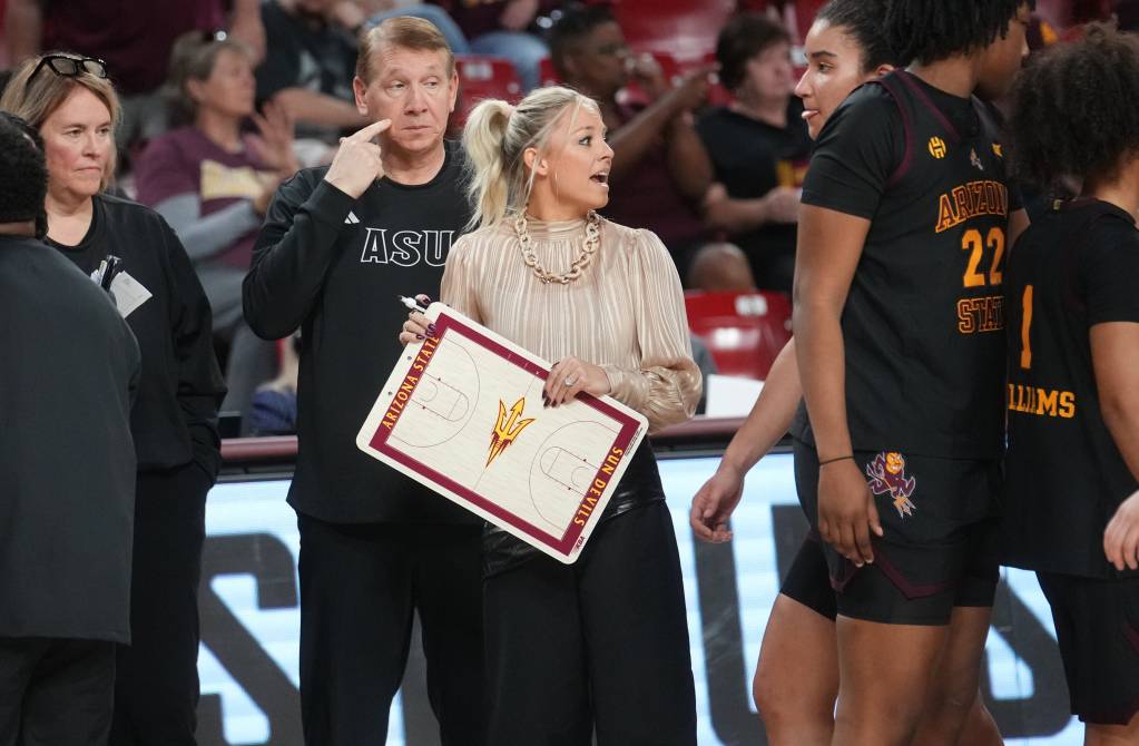 Arizona State coach Molly Miller is holding a clipboard looking into her team's huddle.
