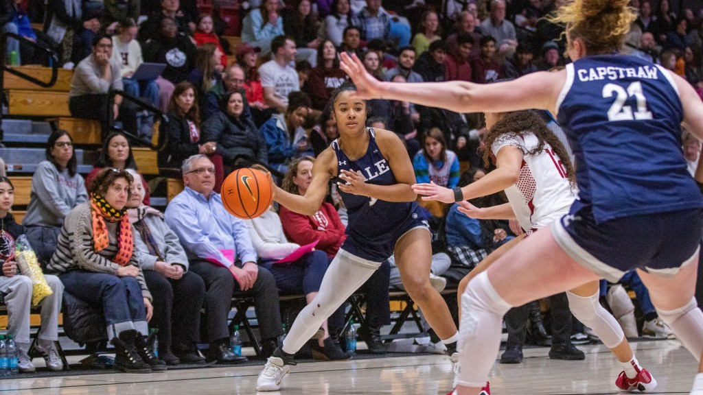 Yale guard Ciniya Moore leans to her right and passes the ball with her right hand. Teammate Kiley Capstraw bends her knees to form a wide base and extends her left arm horizontally to give Moore a target.