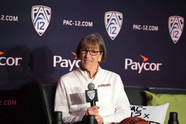 Stanford Cardinal head coach Tara VanDerveer sits and holds a microphone as she speaks at a preseason media day. Pac-12 logos are visible on the backdrop behind her.