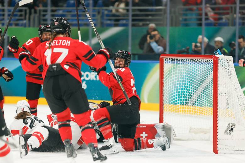 Marie Philip-Poulin is knelt down on one knee celebrating in front of the goal with her teammates.