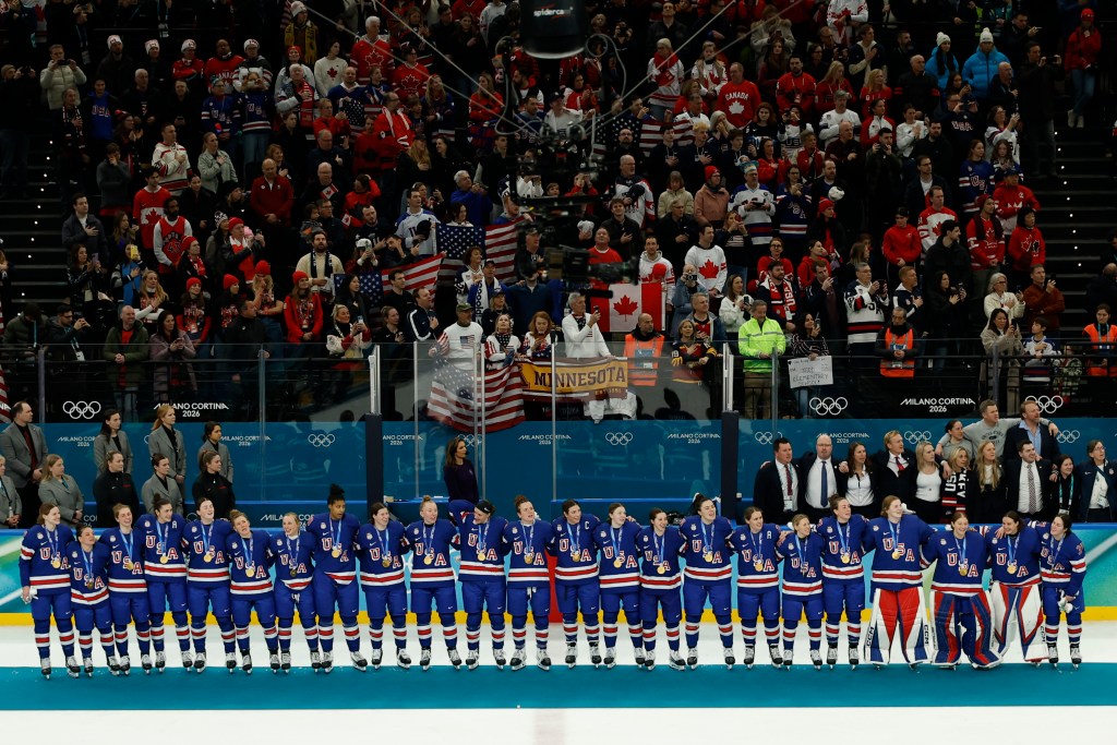 Team USA stands arm and arm with their medals around their necks. They are all wearing blue home uniforms.