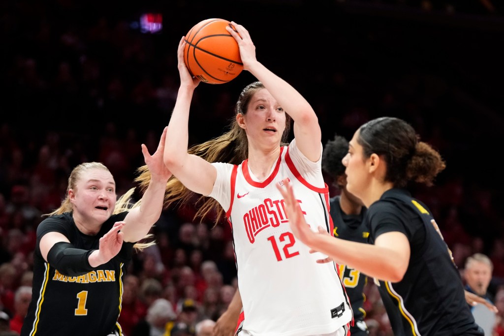 Ohio State Buckeyes center Elsa Lemmilä looks to pass. She has Michigan defenders on either side of her.