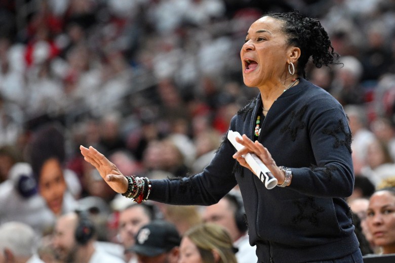 Dawn Staley coaching shouts directions from the sideline while clutching rolled up paper in her hand