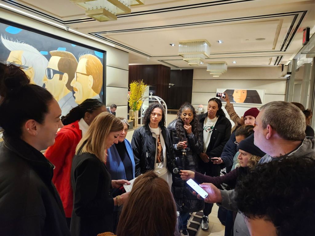 Photo of WNBA commissioner Cathy Engelbert, members of the WNBPA and reporters. Engelbert is reading off a piece of paper she is holding.