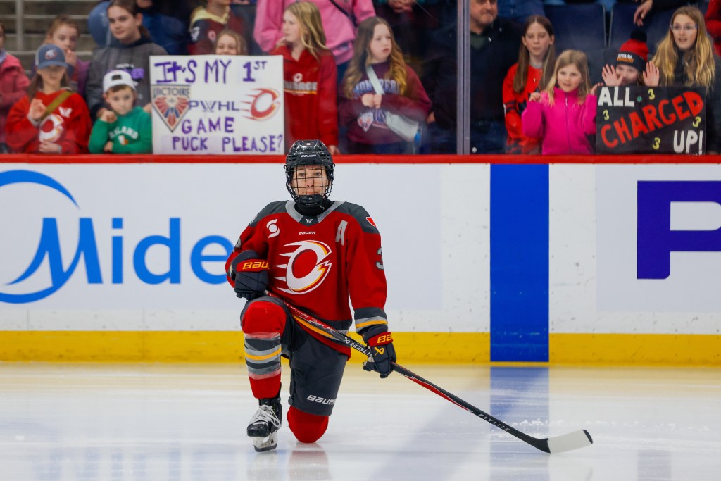 Larocque kneels near the blue line during the first PWHL game in Winnipeg. She is wearing a red home uniform.