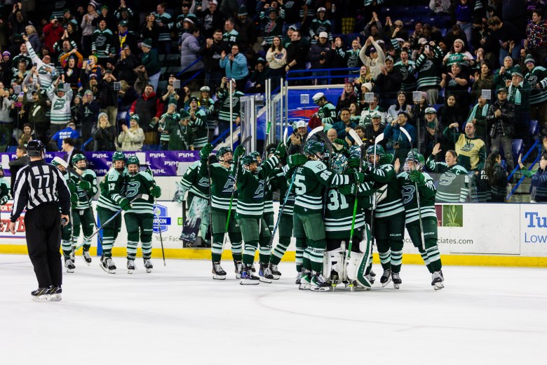Fleet players celebrate on the ice with a big group hug. They are all wearing green home uniforms.